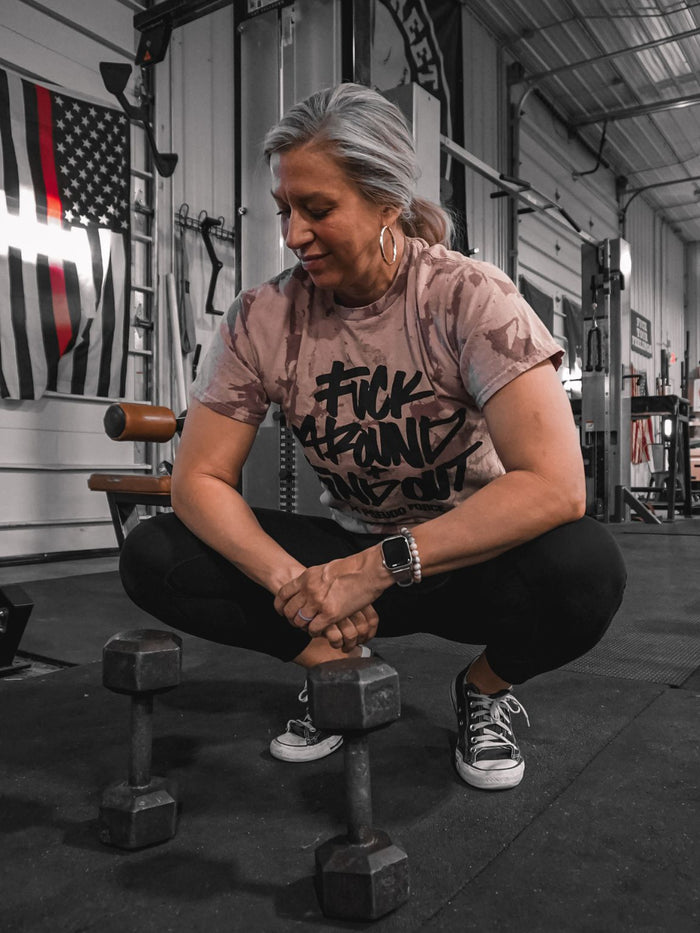 A woman posing in a fuck around and find out pink shirt between bicep curl sets.