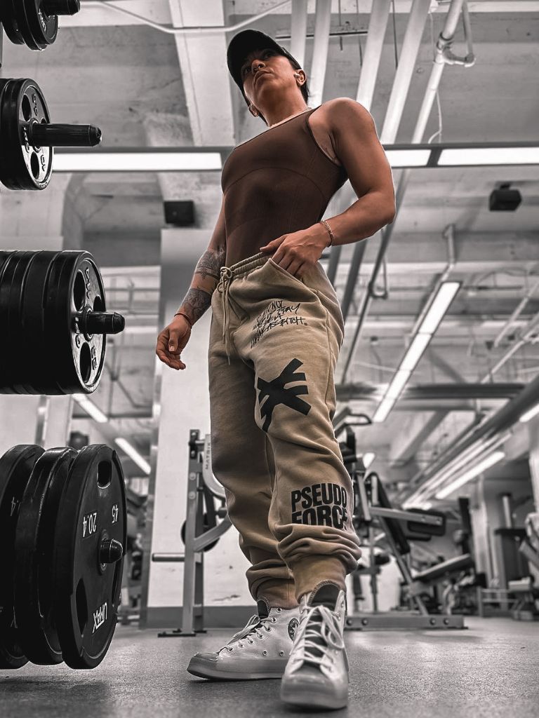 Person in a gym wearing a tank top and tan jogger sweat pants with visible pseudo force branding.