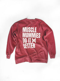Red crewneck sweatshirt laid flat on a white background. Back of the sweatshirt features large white text reading ‘Muscle Mommies Do It Better’ with a Pseudo Force symbol between the words.