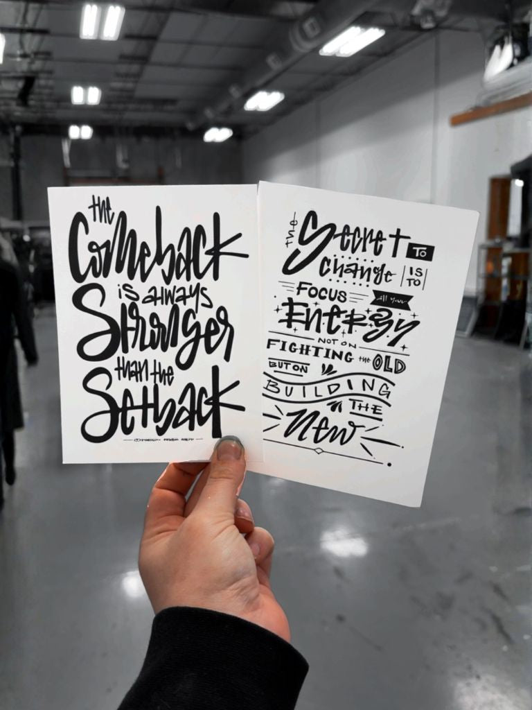 Hand holding two pieces of paper with motivational quotes in an indoor setting.