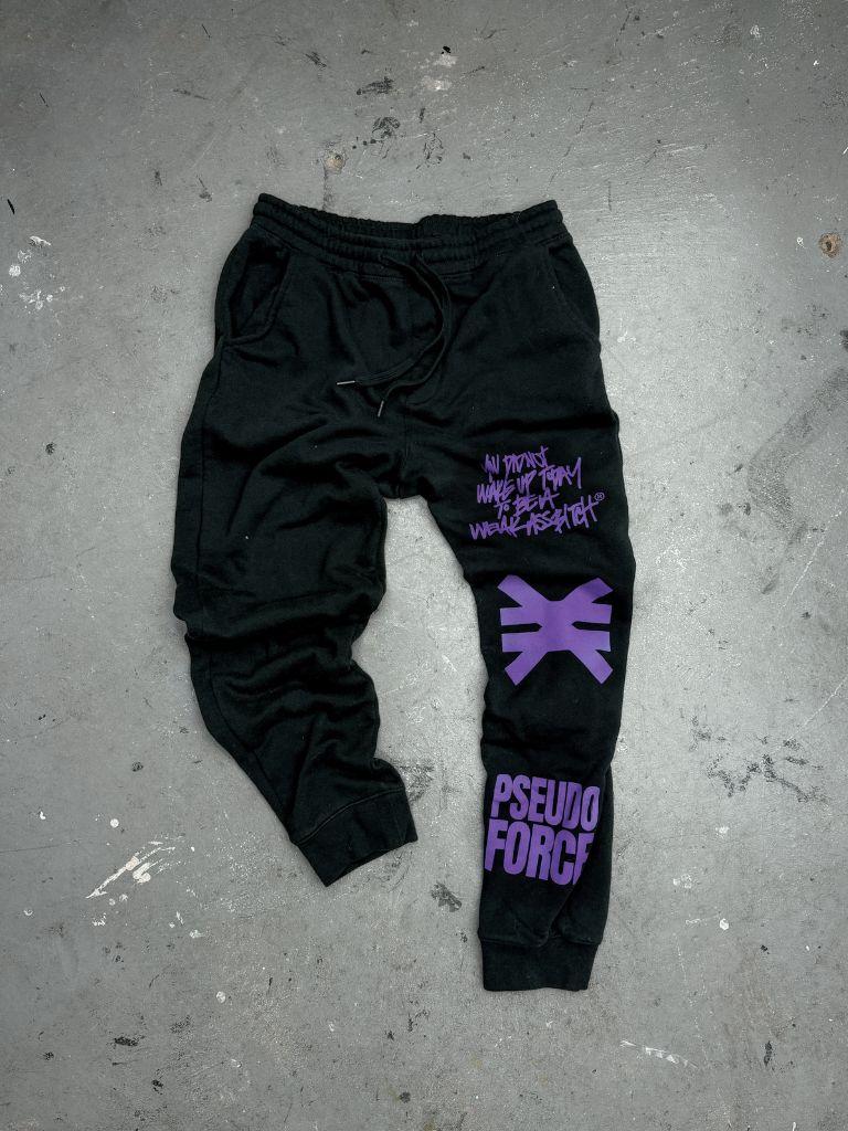 Black sweatpants with purple graphic prints, including the text 'PSEUDO FORGE' and a stylized symbol, laid flat on a gray concrete floor.