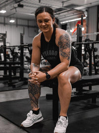 woman on bench at gym in black pseudo force tank