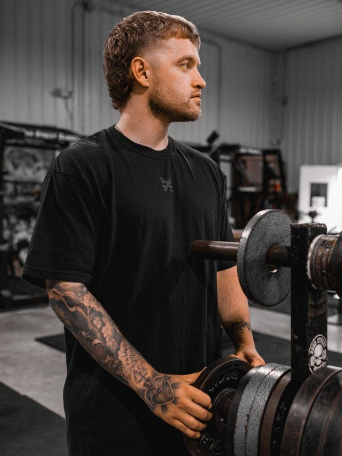 man in gym getting weights in black pseudo force logo shirt