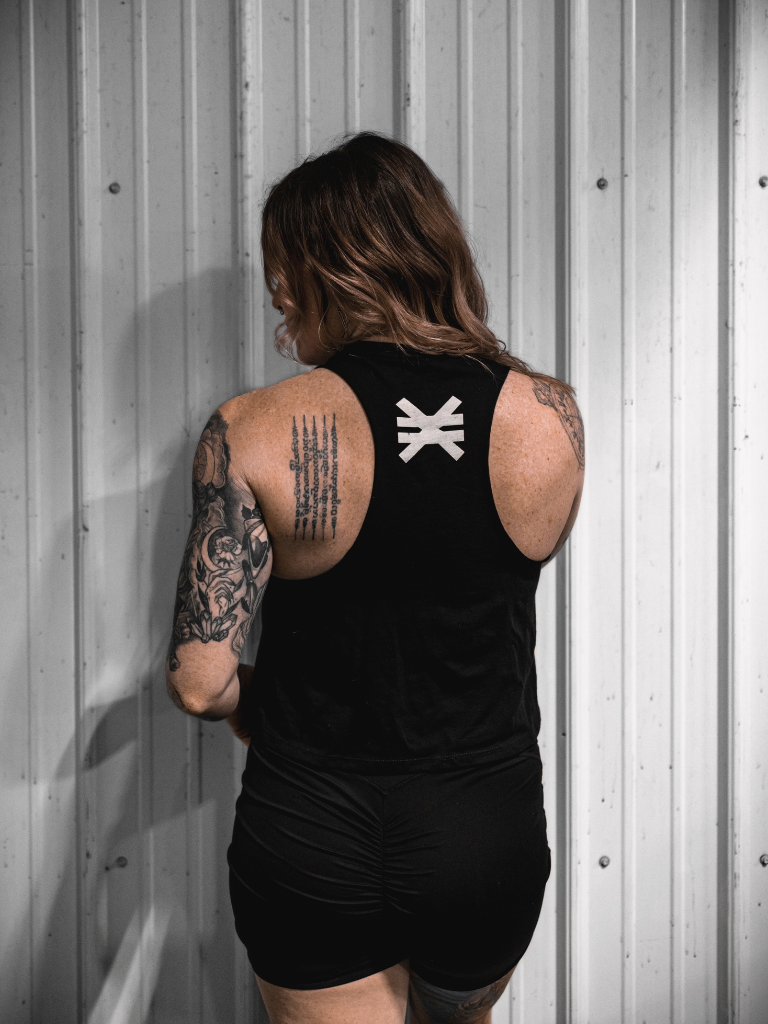 Person wearing a black tank top with a white logo against a metallic wall.