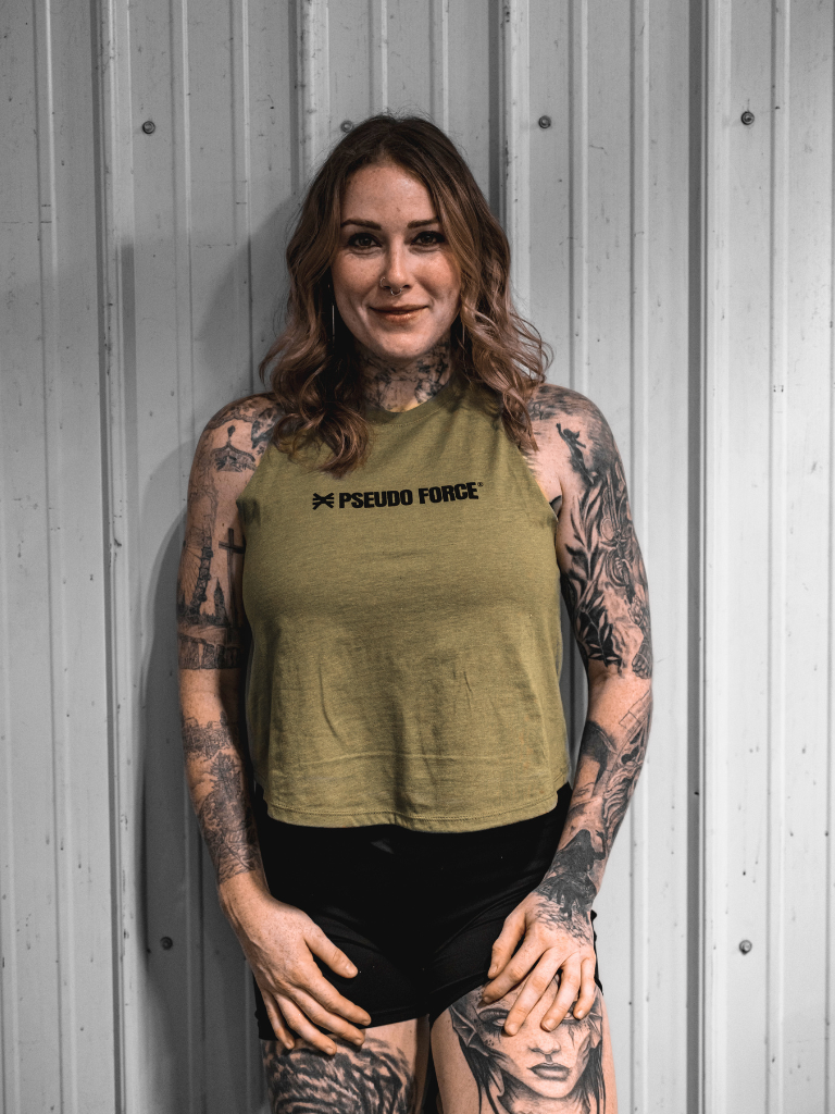 Woman wearing a green tank top with 'Pseudo Force' logo against a gray wall