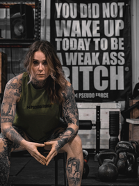 Woman with tattoos wearing a green tank top in a gym setting with motivational poster.