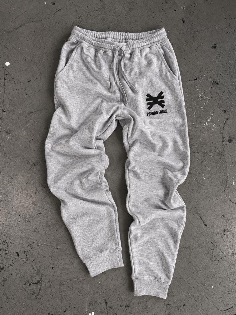 Gray jogger sweatpants with a black pseudo force logo on the left leg. Laying on cement floor with ink splatters.