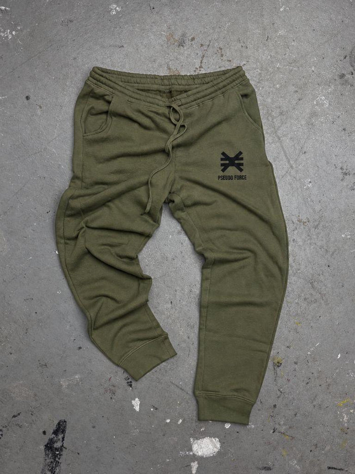 green jogger sweatpants on cement floor with ink splatters. Black Pseudo Force logo on pocket