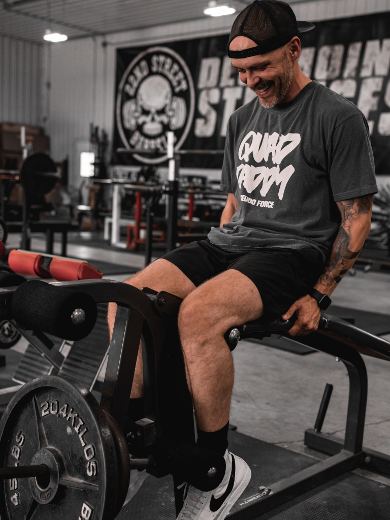 Man sitting on a weight bench in a gym with quad daddy shirt from pseudo force