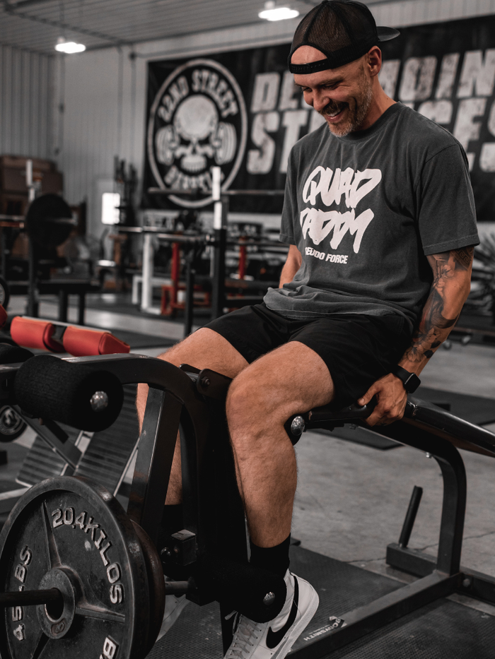 Man sitting on a weight bench in a gym with quad daddy shirt from pseudo force