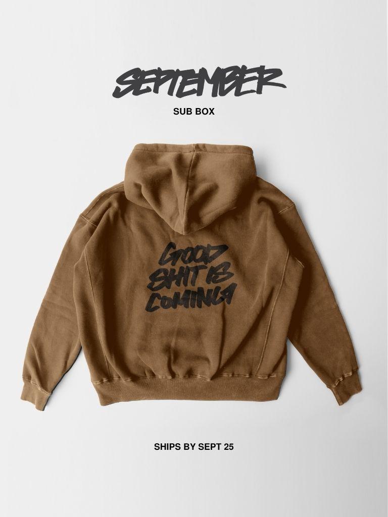 A brown hooded sweatshirt shown from the back on a light gray background, with black text reading 'GOOD SHIT IS COMING' across the back. Above the hoodie, 'SEPTEMBER SUB BOX' is printed, and below, 'SHIPS BY SEPT 25'.