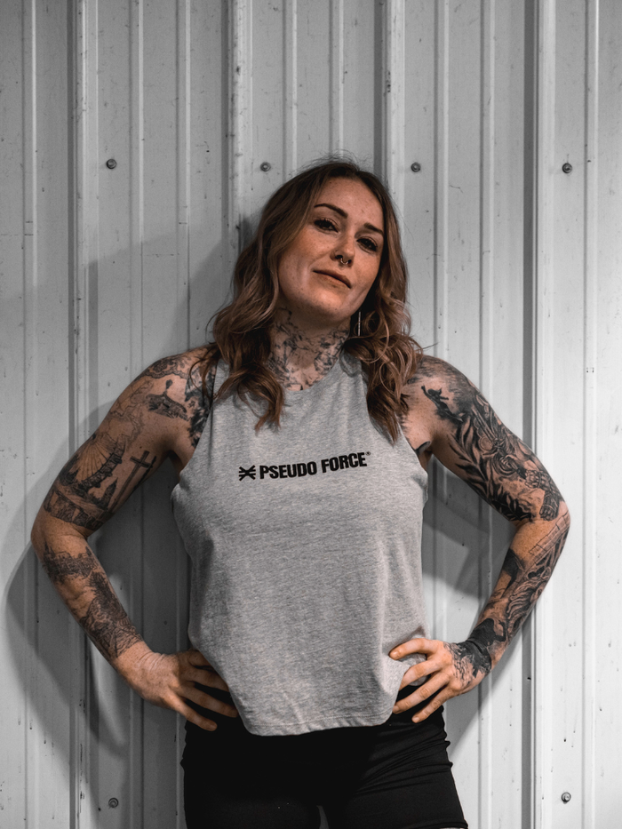 Person wearing a gray tank top with 'Pseudo Force' logo against a metallic wall.