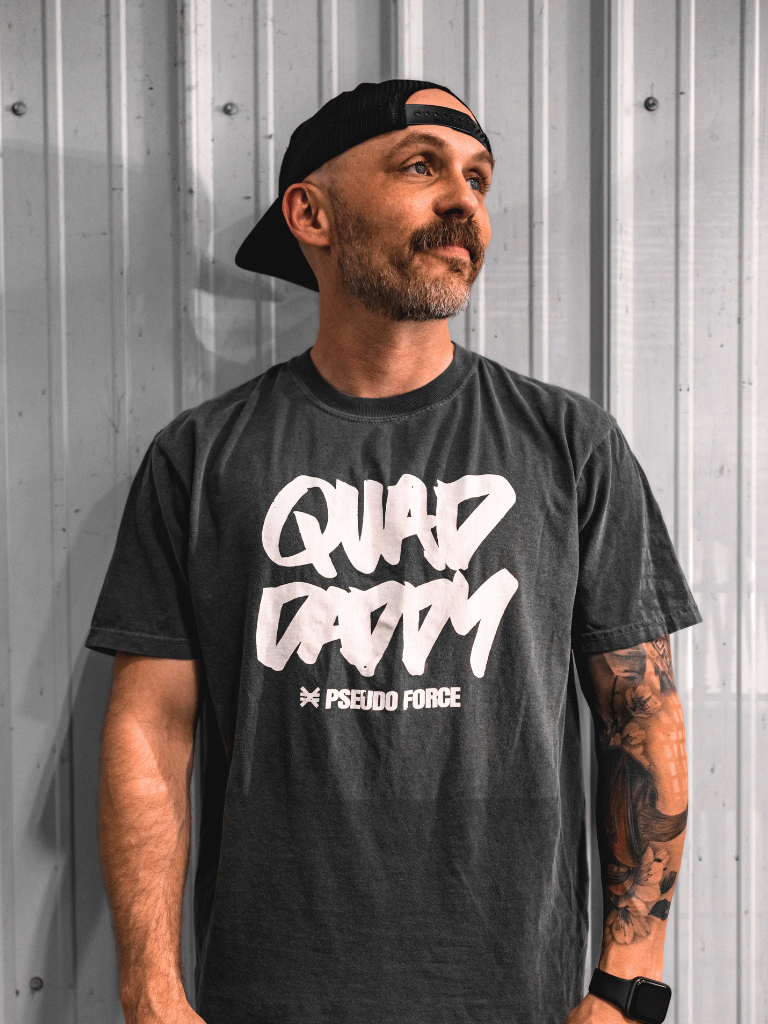 Man wearing a black t-shirt with 'Quad Daddy' in white text against a metallic wall.