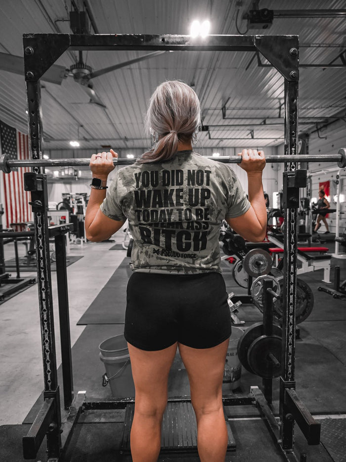 A woman doing shoulder presses wearing a green tie dye shirt that says You Did Not Wake Up Today To Be A Weak Ass Bitch from Pseudo Force.