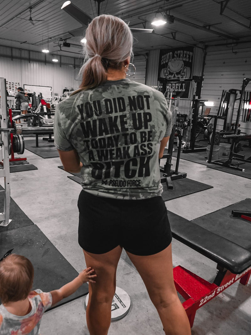 Woman and child at the gym. She is wearing a shirt that says You Did Not Wake Up Today To Be A Weak Ass Bitch from Pseudo Force in a powerlifting gym.
